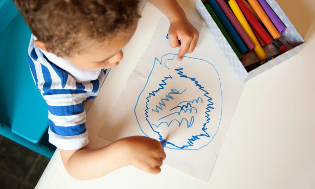 A young child is drawing on paper with crayons.