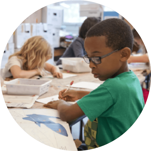 A boy is writing on paper in front of other children.